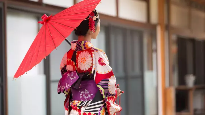Woman in traditional colorful kimono holding red parasol in Japanese setting